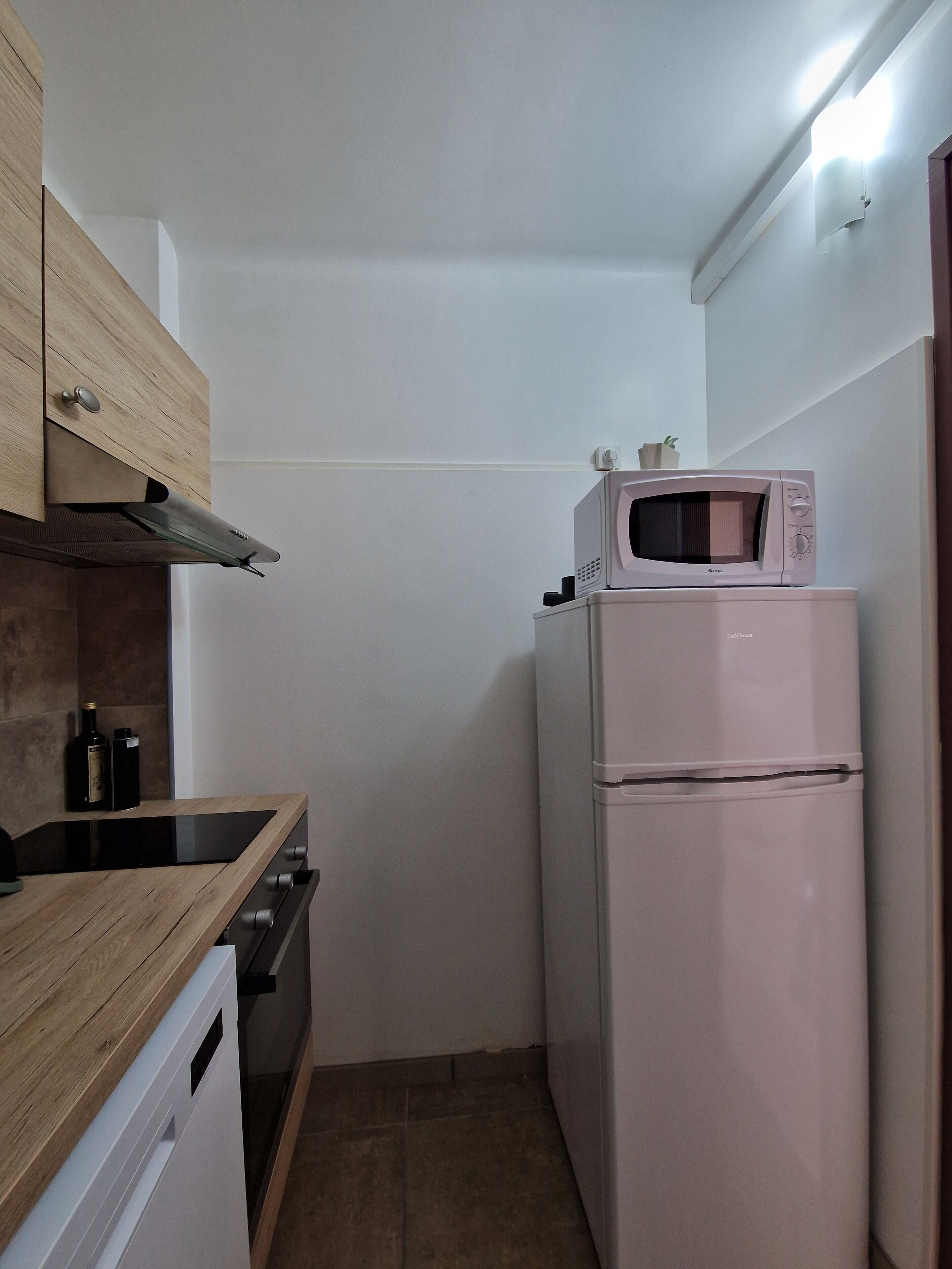 A compact kitchen with a microwave on top of a white refrigerator, a wooden countertop, and a built-in oven.