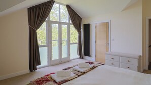 Ein Schlafzimmer mit großem Fenster, einem Bett mit Quiltdecke, einem Nachttisch und einem Kleiderschrank.