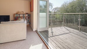 Ein modernes Wohnzimmer mit einer Couch, einem Bücherregal und einem großen Fenster mit Blick auf einen Balkon.