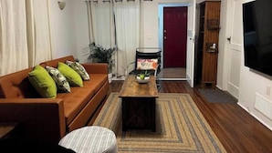 A living room with a brown sofa, a coffee table, and a TV. There is a door leading to another room and a plant in the corner. - The perfect spot/beachfront cozy cottage (Wasaga Beach)