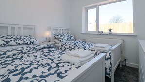 Une chambre avec deux lits, du linge de lit blanc, une fenêtre donnant sur une clôture et un radiateur.