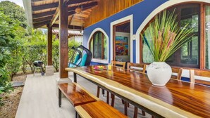 An outdoor dining area with a wooden table and benches, surrounded by a blue wall and large windows. - Tropical Perfection, Includes Kayak, Snorkel, Beach Gear, Walk To The Beach (Playa Potrero)