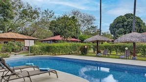 A swimming pool with lounge chairs and umbrellas, surrounded by greenery and buildings. - Tropical Perfection, Includes Kayak, Snorkel, Beach Gear, Walk To The Beach (Playa Potrero)