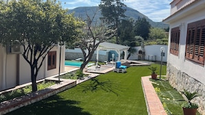 Un césped cuidado con un sendero de ladrillo, una zona de piscina y una montaña al fondo.