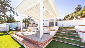 Un patio techado al aire libre con zona de barbacoa, asientos y un muro de piedra.