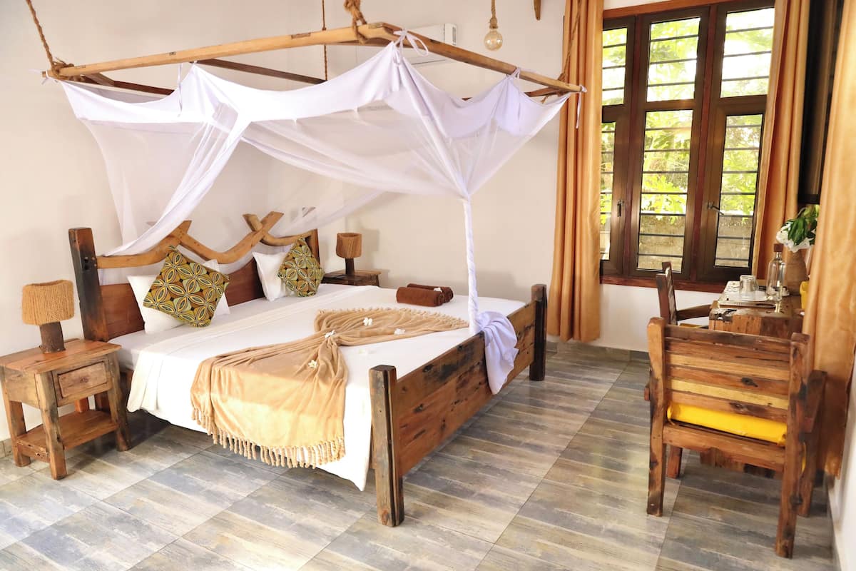 A wooden bed with a canopy, a nightstand, a chair, and a window with curtains.