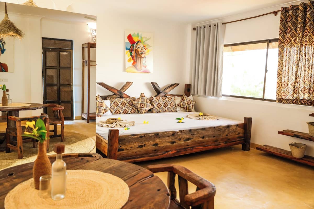 A rustic bedroom with a wooden bed, a dining area with a round table, and a large window with curtains.
