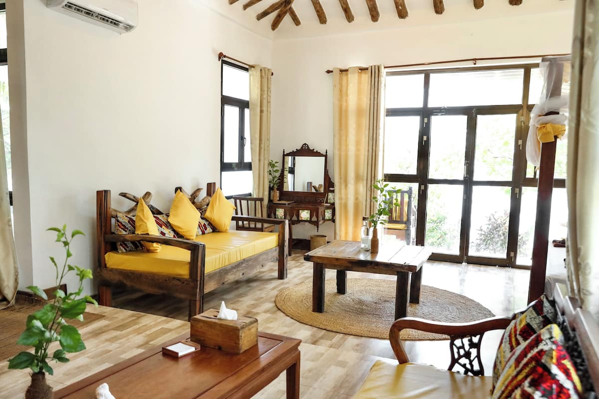 A cozy living room with a wooden sofa, a coffee table, and a large window with curtains.