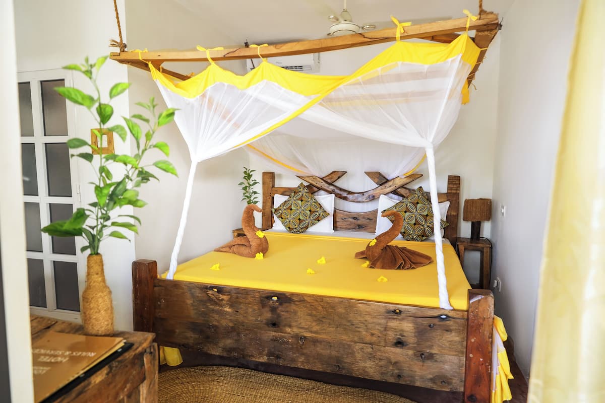 A bed with a yellow bedspread, a wooden headboard, and a canopy with yellow and white fabric.
