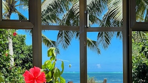 A wooden table with a vase of red flowers and a bowl of eggs in a tropical setting with a view of the ocean. - Z-Lodge Zanzibar (Kiwengwa)
