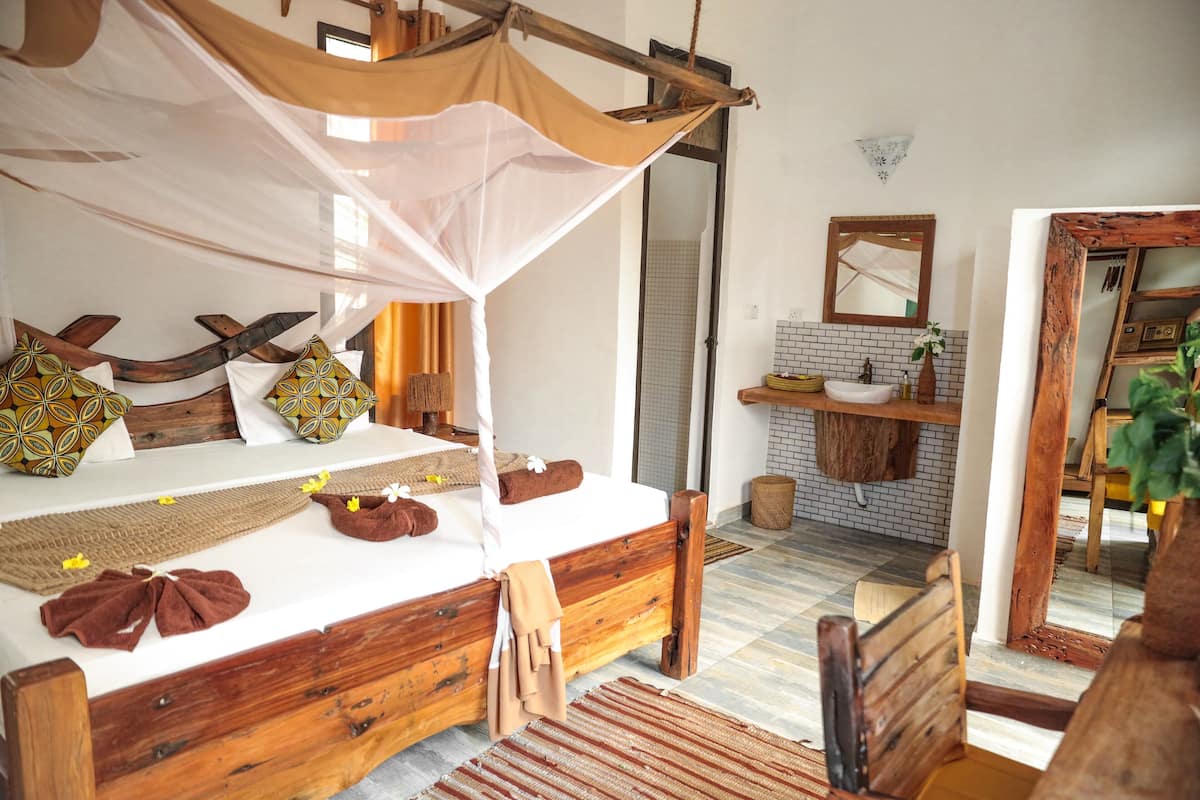 A wooden bed with a canopy, a small bathroom with a sink and mirror, and a wooden chair.
