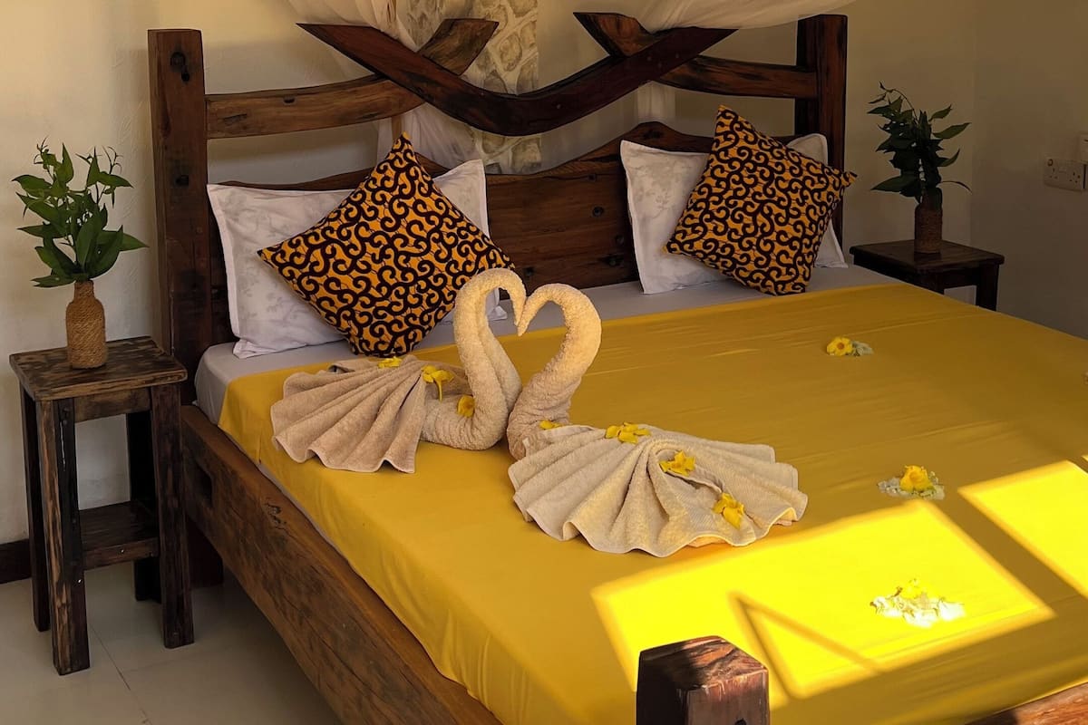 A bed with a yellow bedspread, white pillows, and a canopy. There are two decorative swans made of towels on the bed.