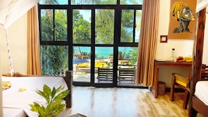 A room with a large window overlooking a beach, a bed, a desk, and a chair. - Z-Lodge Zanzibar (Kiwengwa)