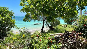 A tropical beach with clear turquoise waters, a boat, and lush greenery. - Z-Lodge Zanzibar (Kiwengwa)