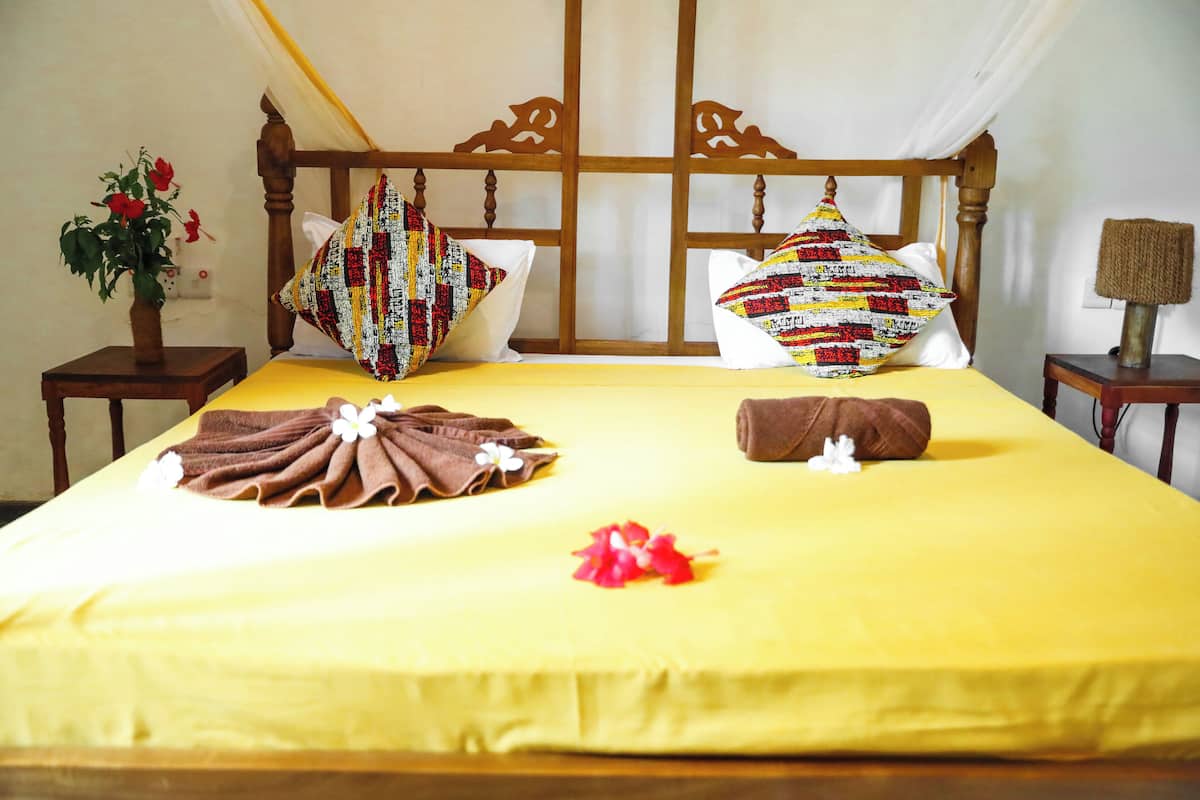 A neatly made bed with a yellow bedspread, two pillows with patterned covers, and a brown towel folded on the bed.