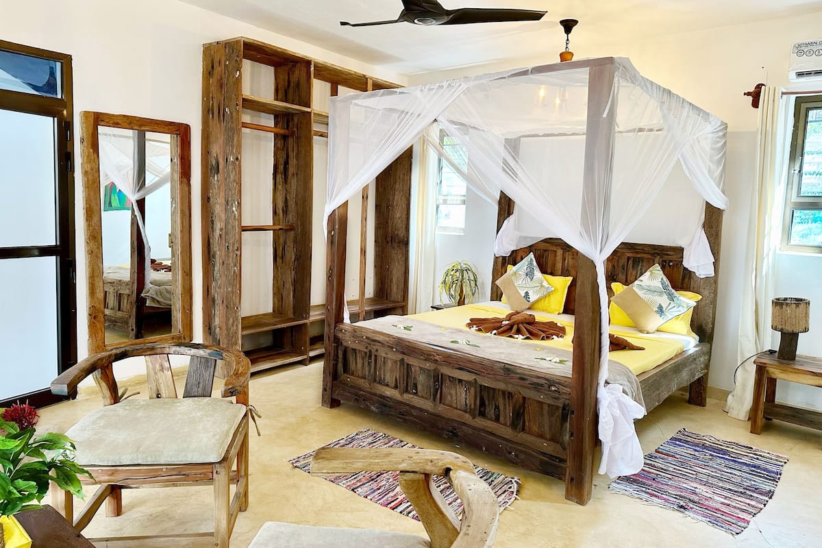 A rustic wooden four-poster bed with a canopy, a wooden chair, and a small table with a plant.