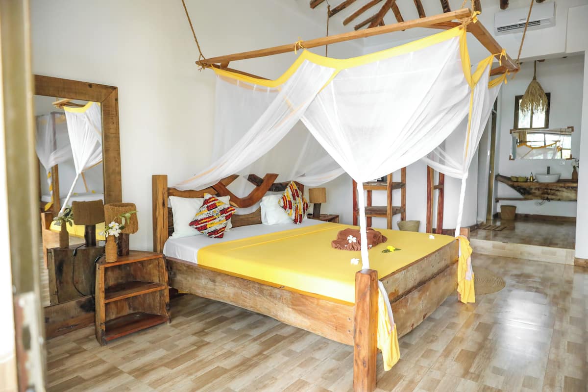 A wooden bed with a yellow mattress, white net canopy, and wooden headboard.