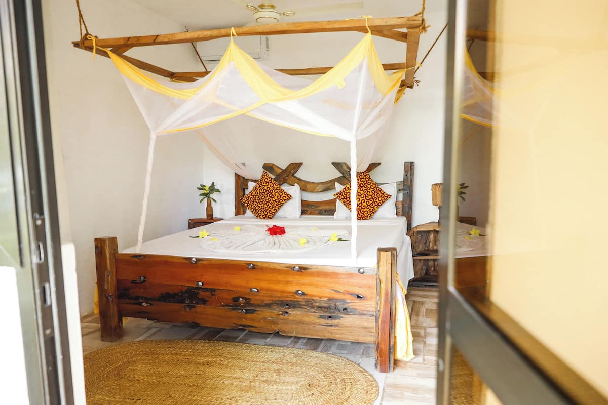 A bed with a wooden frame and a canopy, a bedside table, and a small plant.
