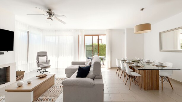 A modern living room with a sofa, coffee table, and TV. There's a dining area with a table set for four. - Charming Villa Óbidos by LovelyStay (Nadadouro)
