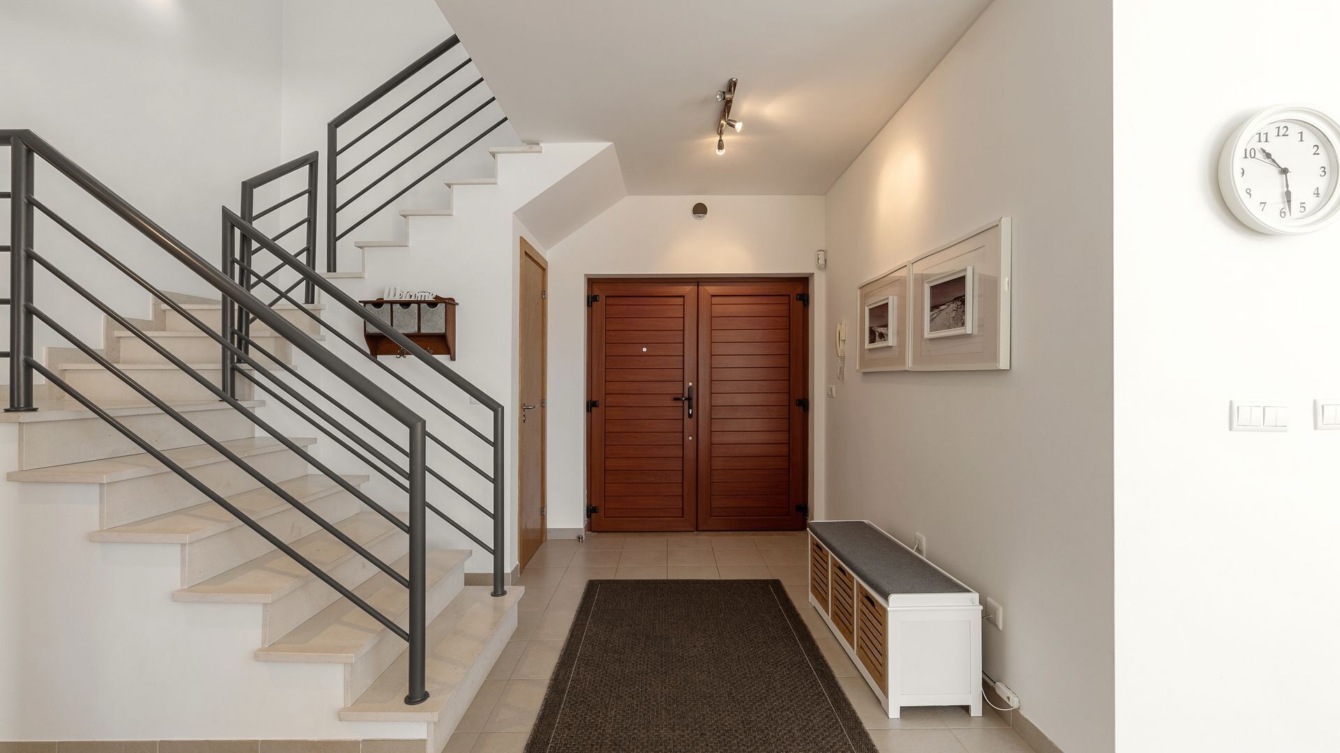 A staircase with a metal railing, a wooden door, a bench, and a wall-mounted clock.