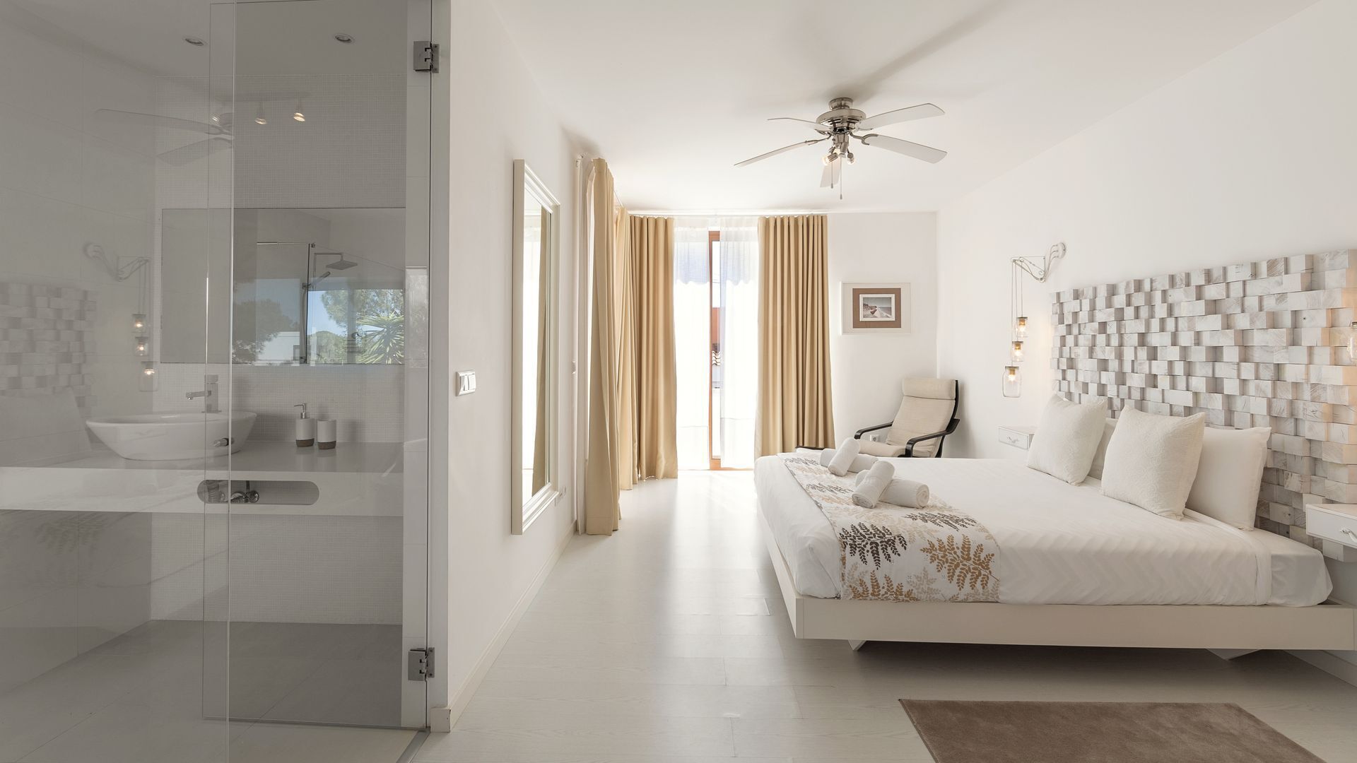 A modern bedroom with a large bed, a ceiling fan, and a view of the outdoors through a glass door.