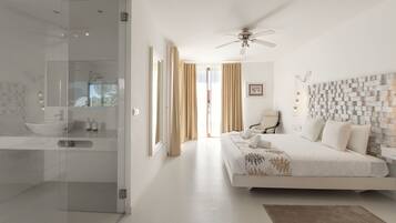 A modern bedroom with a large bed, a ceiling fan, and a view of the outdoors through a glass door.