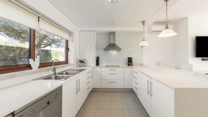A modern kitchen with white cabinetry, a built-in dishwasher, a stove, and a coffee maker. There is a window with a view of greenery outside. - Charming Villa Óbidos by LovelyStay (Nadadouro)