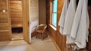 A wooden cabin room with a wooden bench, a chair, and towels hanging on a rack. - 15min to Pictured Rocks|Secluded Cabin w/Sauna (Wetmore)