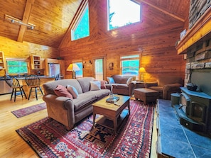 A cozy cabin interior with a fireplace, wooden walls, a sofa, and a dining area. - 15min to Pictured Rocks|Secluded Cabin w/Sauna (Wetmore)