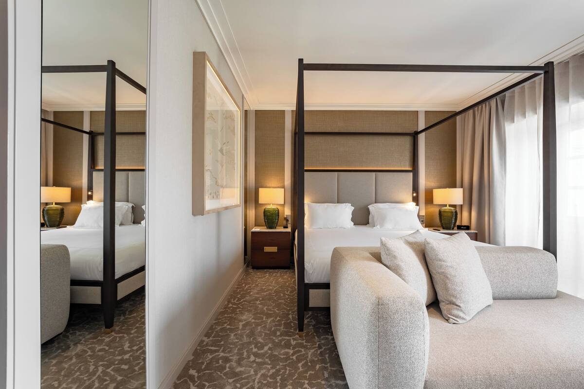 A four-poster bed with a headboard, a sofa, and a nightstand with a lamp.