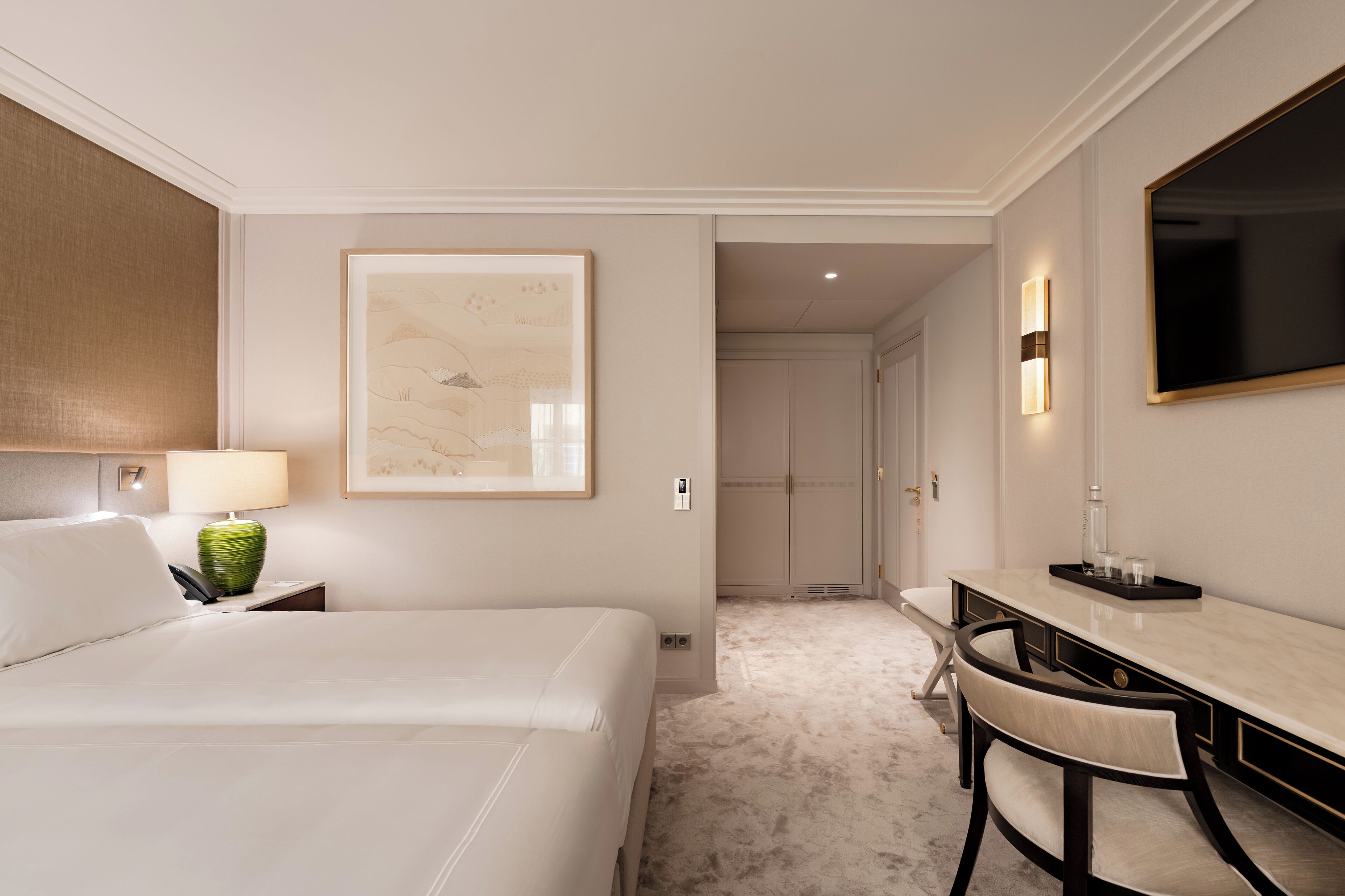 Habitación de hotel con cama, escritorio, silla, lámpara, cuadro enmarcado y televisor.