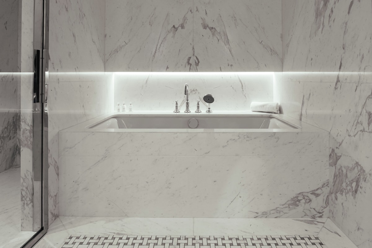 Un baño moderno con lavamanos de mármol, cabina de ducha de vidrio y suelo estampado.