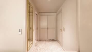 A narrow hallway with a marble floor, a large mirror on the left, and a door at the end.