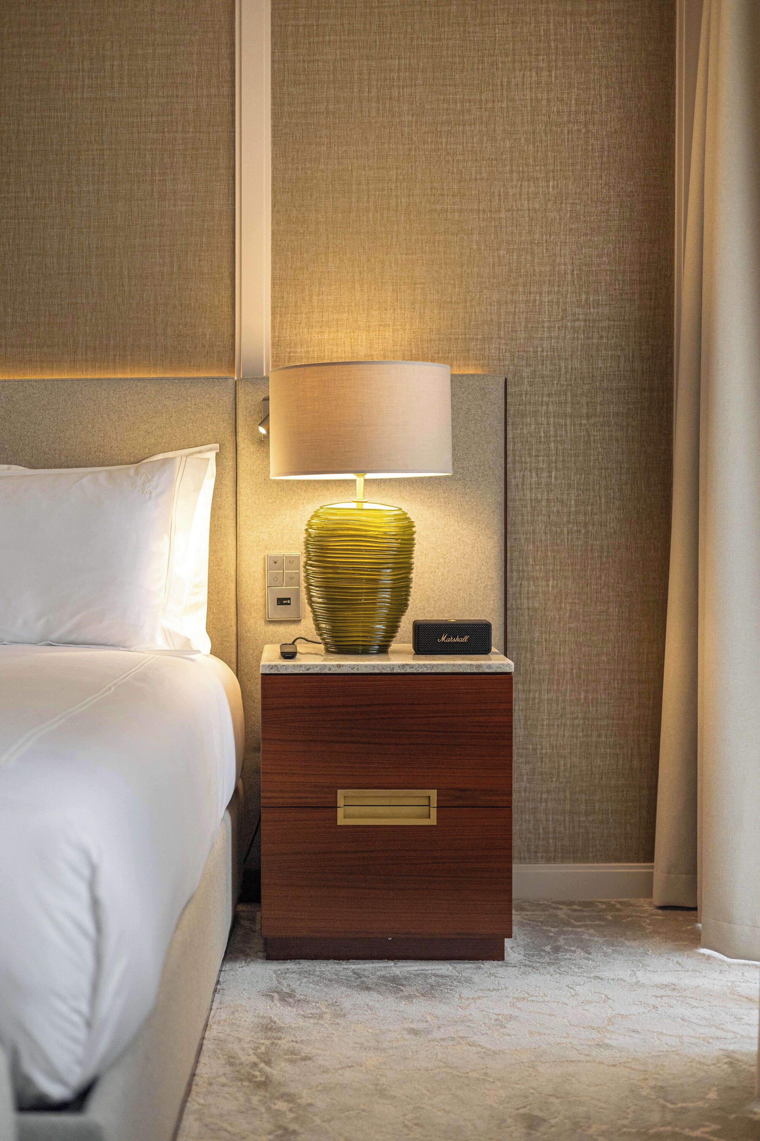 Una habitación de hotel impecable con una cama, una lámpara de noche, una mesita de noche y una lámpara de pared.