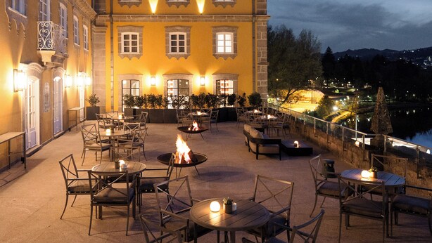 A courtyard with outdoor seating and a fire pit, surrounded by a building with multiple windows and warm lighting. - Casa da Calçada Relais & Châteaux (Amarante)