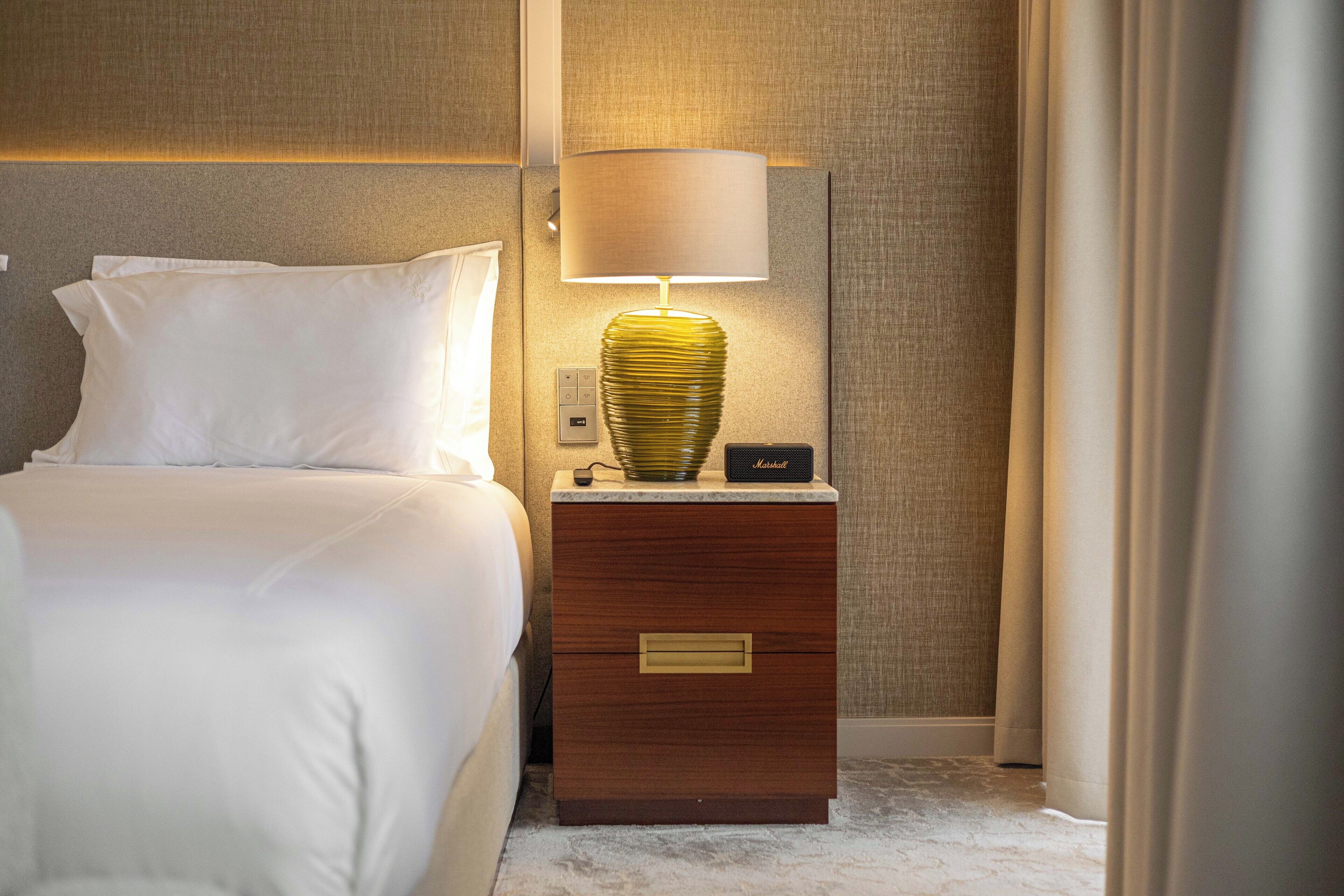 A neatly made hotel room with a bed, a bedside lamp, and a nightstand with a lamp.