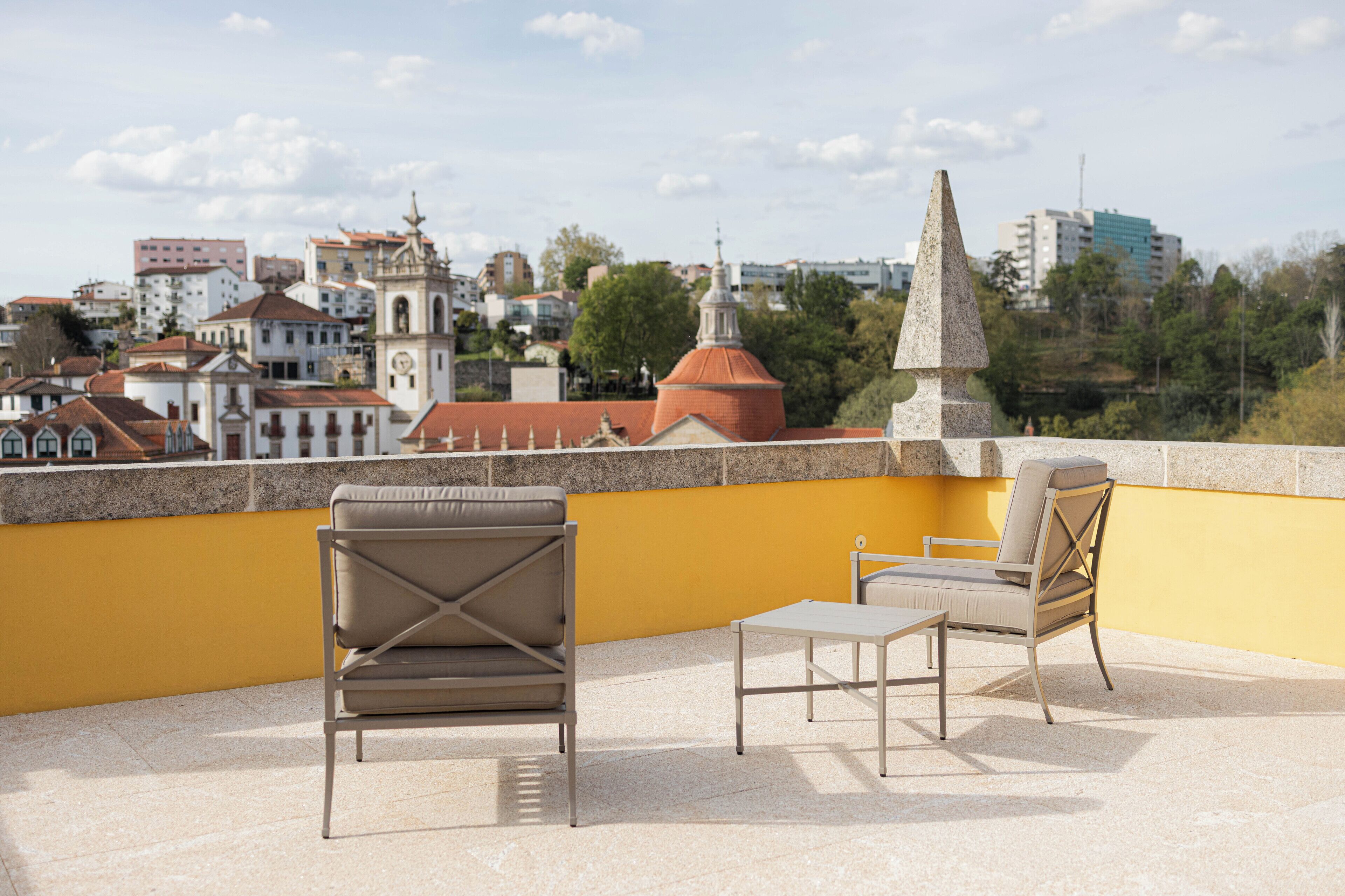 A rooftop terrace with two chairs and a table, overlooking a cityscape with historic buildings and a church.