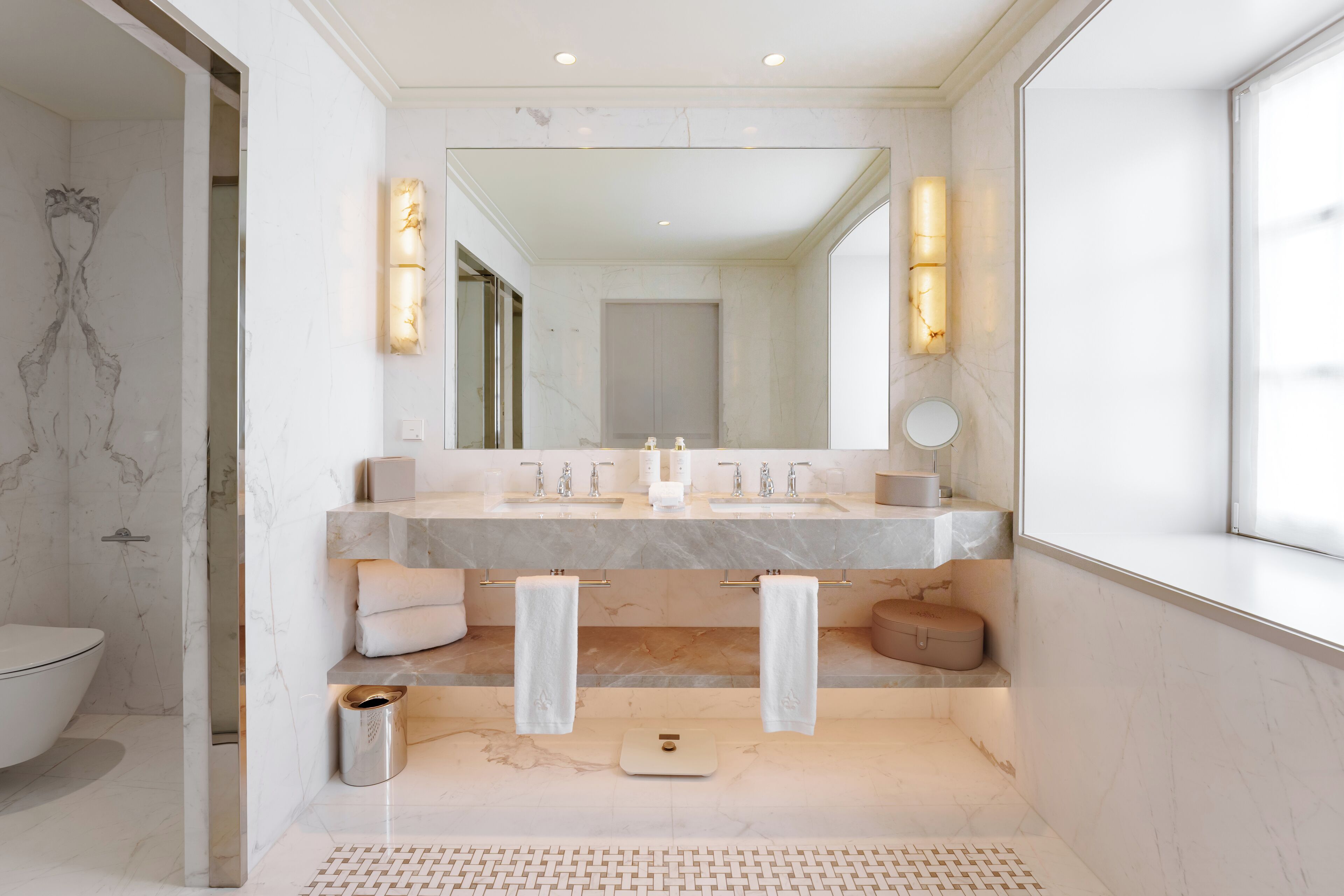 Een moderne badkamer met een grote spiegel, twee wasbakken en een weegschaal.