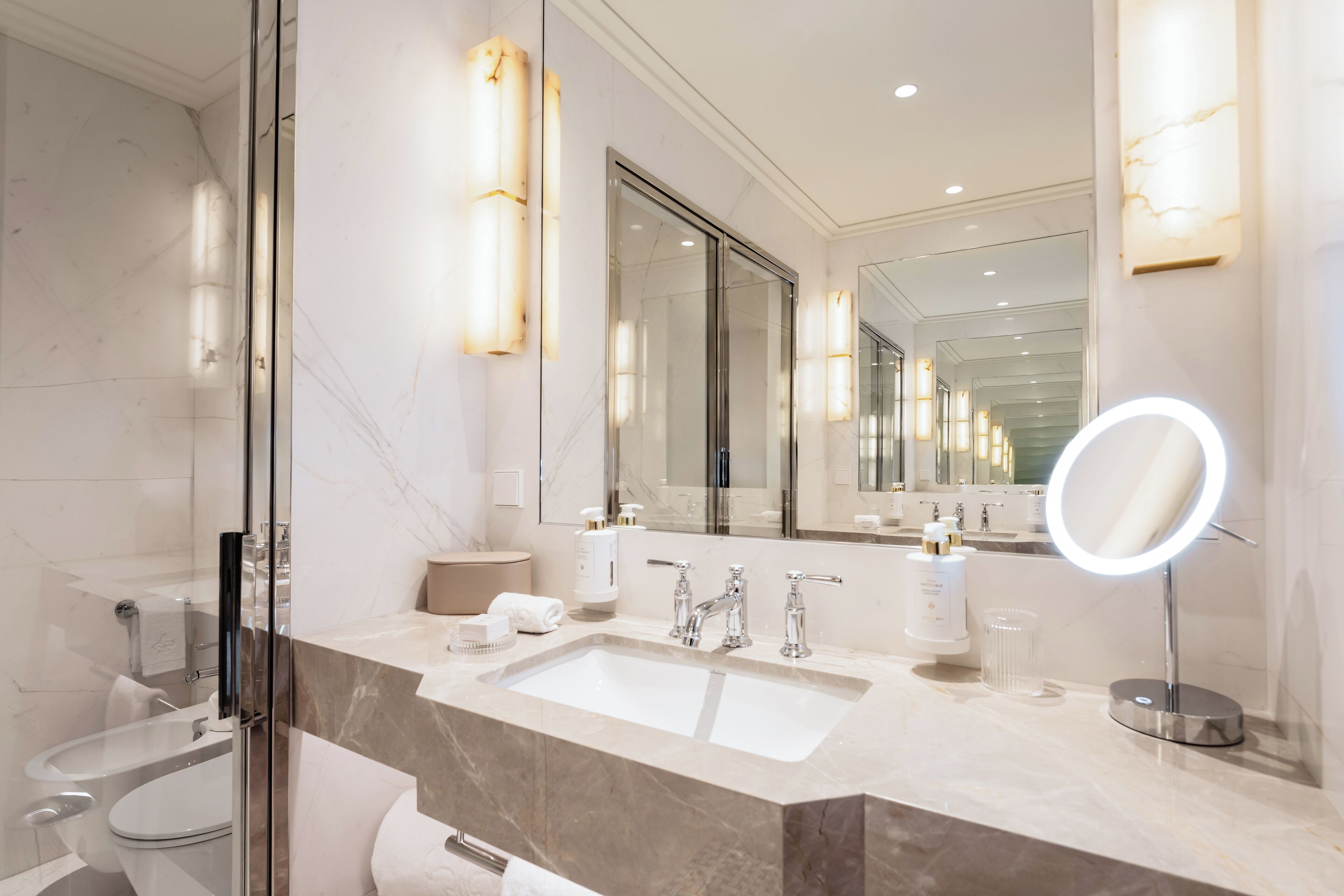A modern bathroom with a glass-enclosed shower, a large mirror, and a vanity with a sink and multiple toiletries.