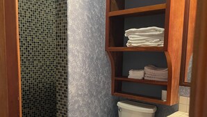 A bathroom with a toilet, a sink, and a shelf with folded towels.