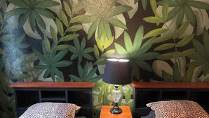 A room with two beds, each with leopard print bedding, a nightstand with a lamp, and a wall mural of green leaves.