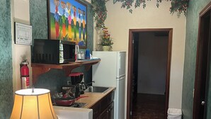 A compact kitchen with a microwave, stove, sink, and refrigerator. A painting is on the wall, and there's a door leading to another room.