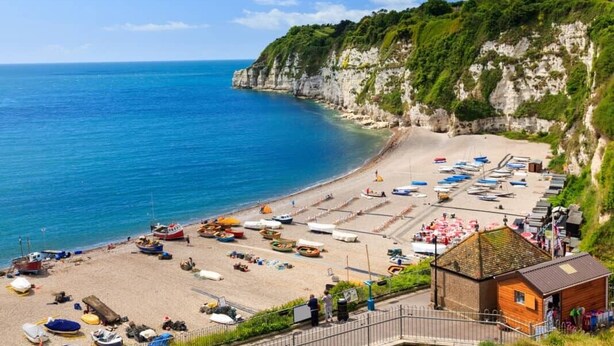 Une plage côtière avec des bateaux, une petite construction en bois et une falaise.