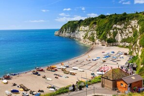 A coastal beach with boats, a small wooden structure, and a cliff.