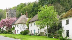 Une rangée de charmantes maisons blanches aux toits de chaume, une église en pierre et une végétation luxuriante.