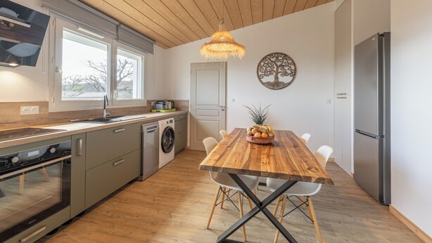 A modern kitchen with a wooden ceiling, stainless steel appliances, and a dining area with a wooden table and chairs. - Comfortable nature gîte with swimming pool, ideal for 2 people, pet-friendly (Salazac)