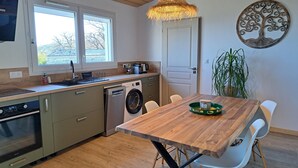 A modern kitchen with a wooden table, built-in appliances, and a large window. - Comfortable nature gîte with swimming pool, ideal for 2 people, pet-friendly (Salazac)