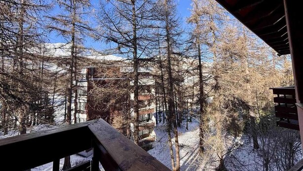 Un paysage enneigé avec des arbres sans feuilles et un bâtiment doté de nombreux balcons.