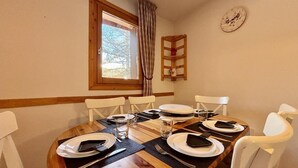 Une table à manger dressée pour quatre personnes, avec des chaises blanches, une table en bois et une fenêtre avec des rideaux.