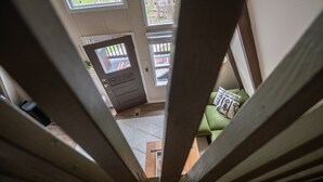 A view through a wooden frame to a room with a green sofa, a wooden table, and a door leading outside.